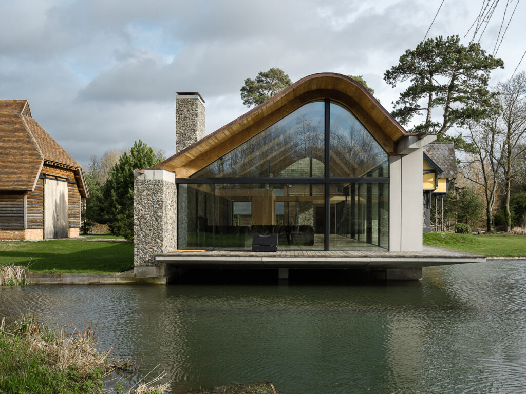 External view of the modern development of a glass stone structure on a lake that is Grade II listed farmhouse, KH House